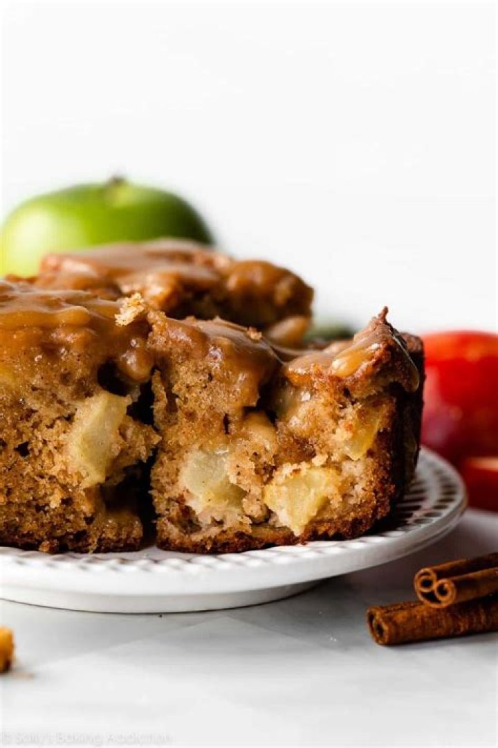 A slice of apple cake on a white plate topped with caramel sauce.